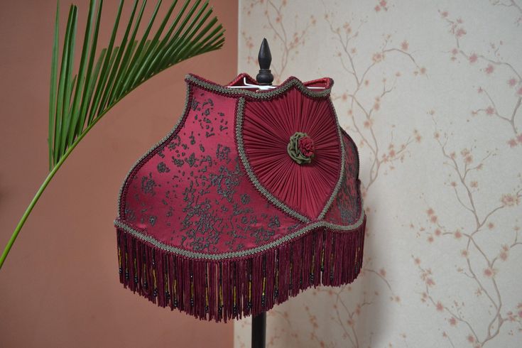 a pink lamp shade on a stand next to a wallpapered wall and palm tree