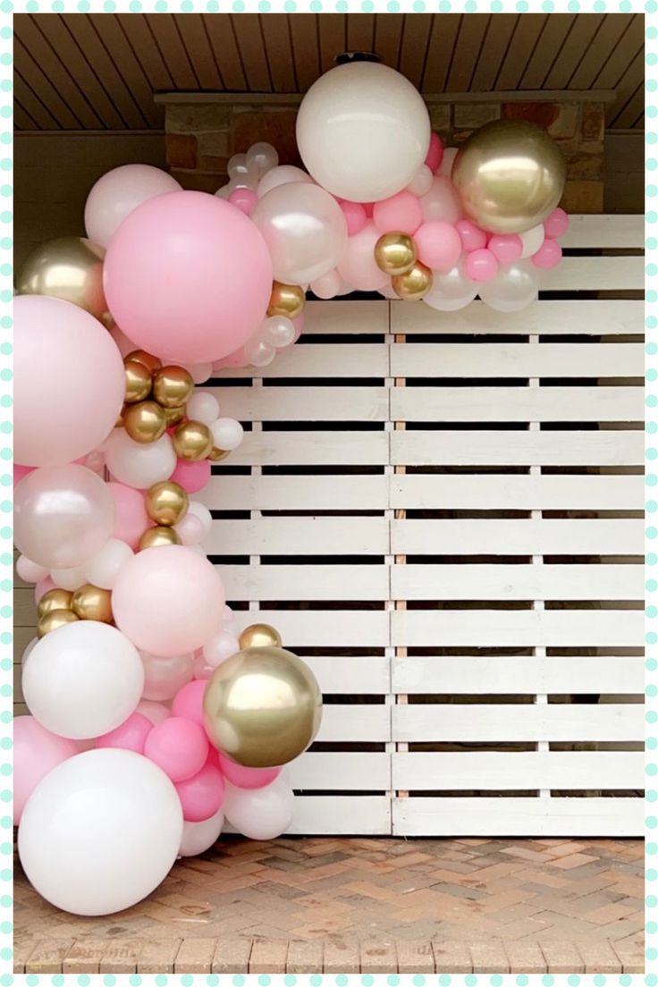 a pink and gold balloon arch with white balloons