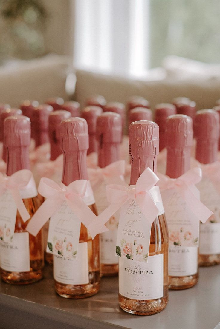 several bottles of wine are lined up on a table with pink bows and ribbons around them