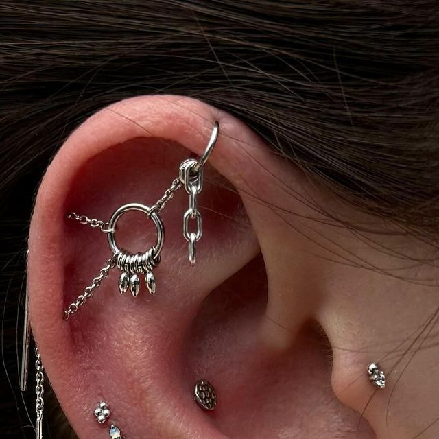 an ear with several piercings attached to it's sides and chains hanging from the side