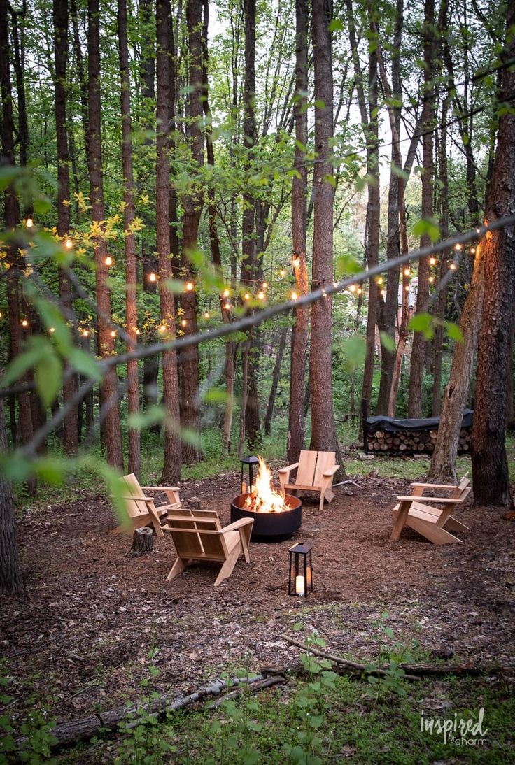 a fire pit surrounded by chairs and lights in the woods