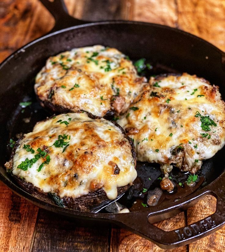 three cheese covered patties in a skillet on a wooden table with utensils