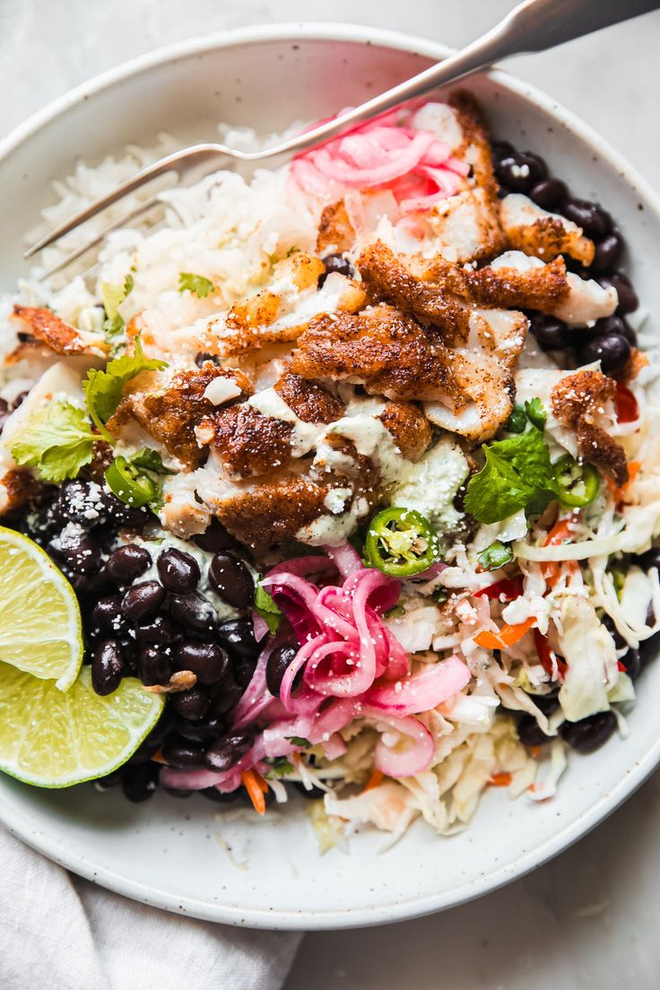 a white bowl filled with rice, black beans and lime wedges next to a fork