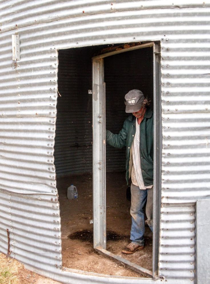 a man standing in the doorway of an old metal building with his hand on the door