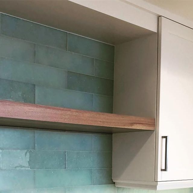 a kitchen with blue tiles and wooden shelves above the stove top, along with white cupboards