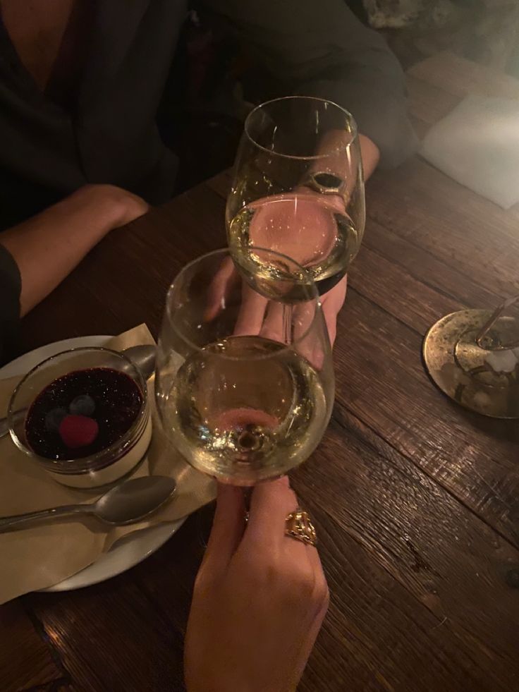 two people holding wine glasses over a wooden table