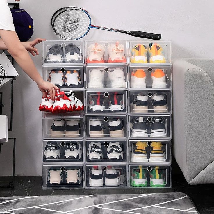 a person holding a racket in front of a wall filled with shoes and tennis racquets