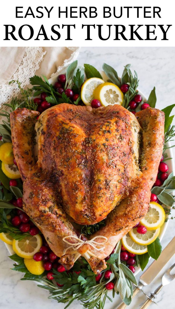 a roasted turkey on a platter with lemons, cranberries and herbs