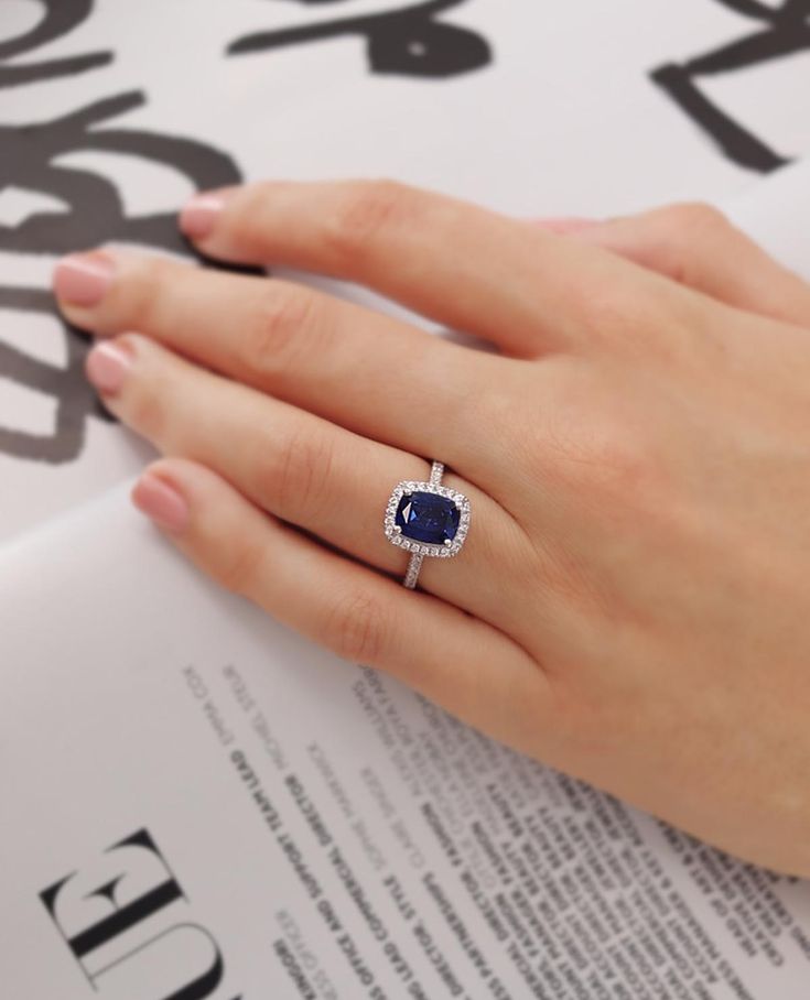 a woman's hand holding an open book with a ring on top of it