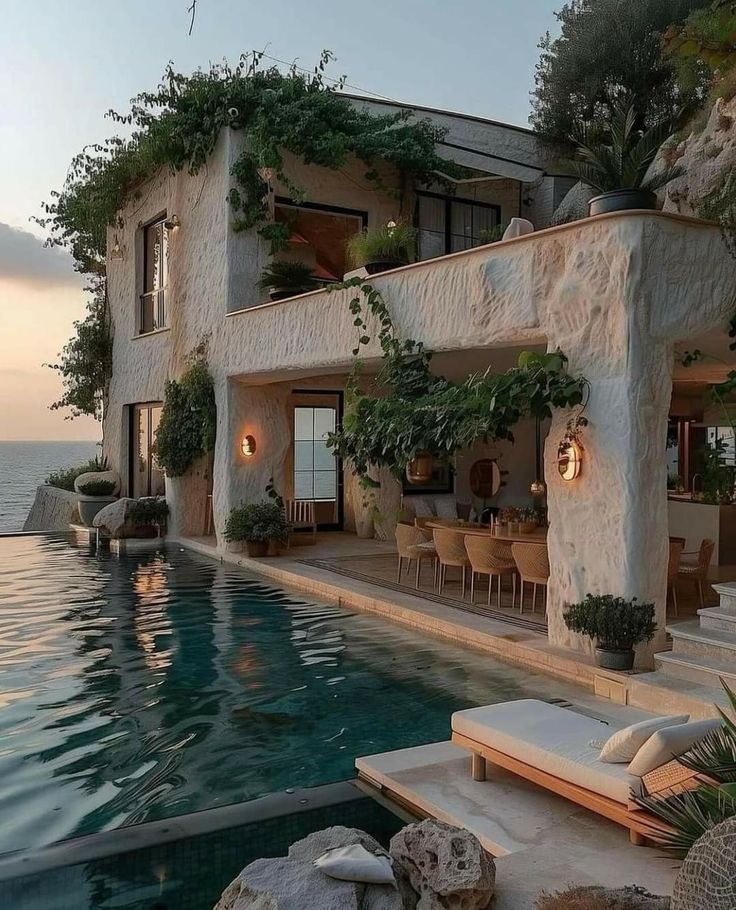 an outdoor pool with chairs and tables next to the ocean at sunset or sunrise time