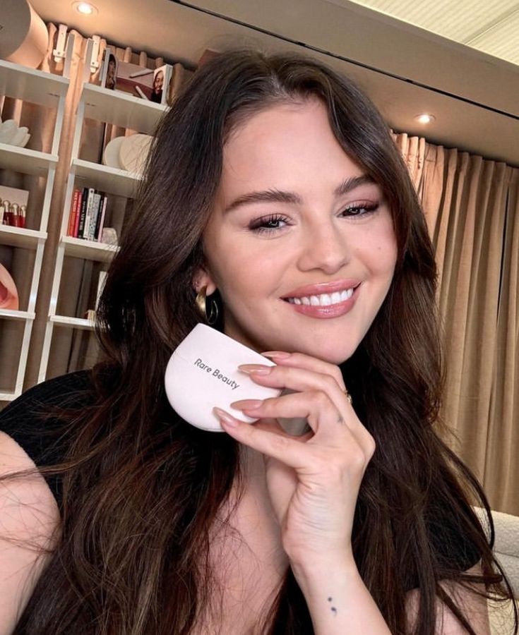 a woman with long brown hair is holding a white object in her hand and smiling