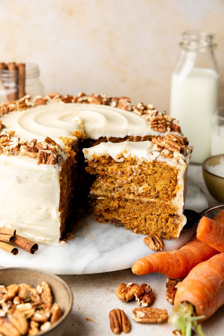 carrot cake with white frosting and chopped nuts on plate next to sliced carrots