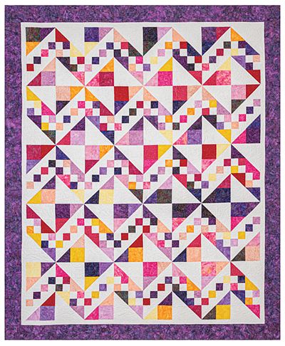 a quilt made with squares and triangles on the front, in purples and reds