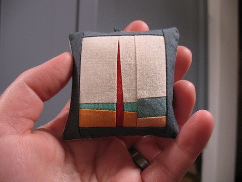 a hand holding a small piece of art made out of fabric and cloth with a red sail on it