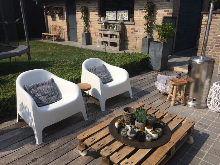 two white chairs sitting on top of a wooden pallet next to a table filled with potted plants