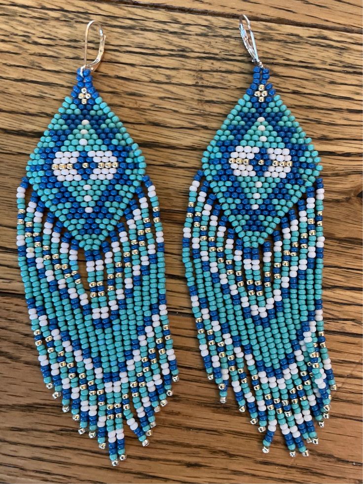 two pairs of beaded earrings with blue and white beads on wooden table next to each other