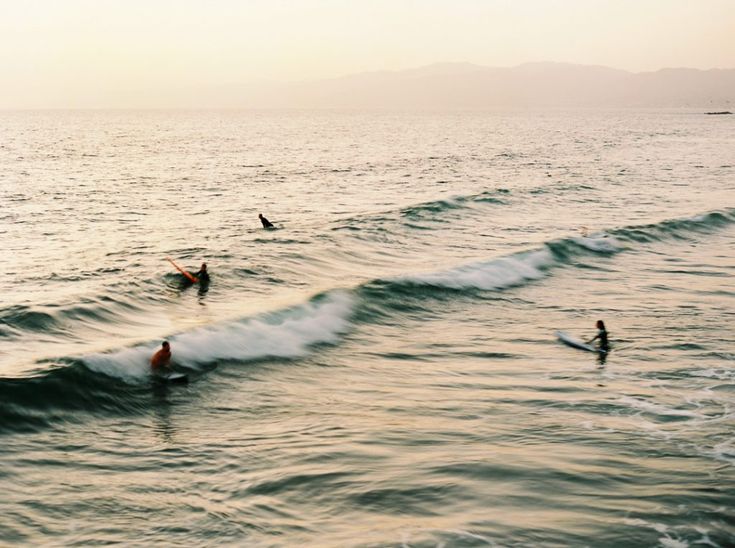 several surfers are riding the waves in the ocean at sunset or dawn, with mountains in the distance