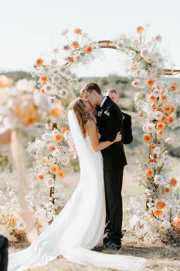 a bride and groom kissing in front of an arch with flowers