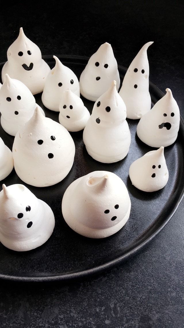 a black plate topped with lots of white frosted halloween ghost candies on top of a table