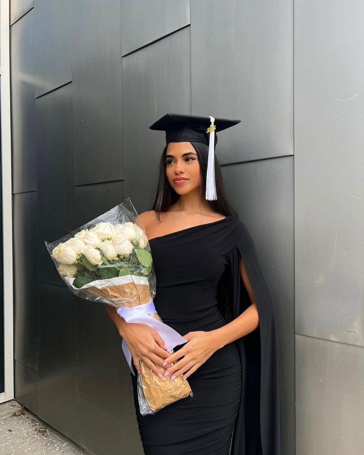 a woman in a graduation gown holding flowers and a bouquet with her hand on her hip