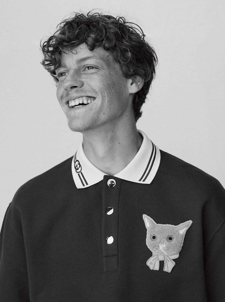 a young man with curly hair wearing a black and white polo shirt smiling at the camera