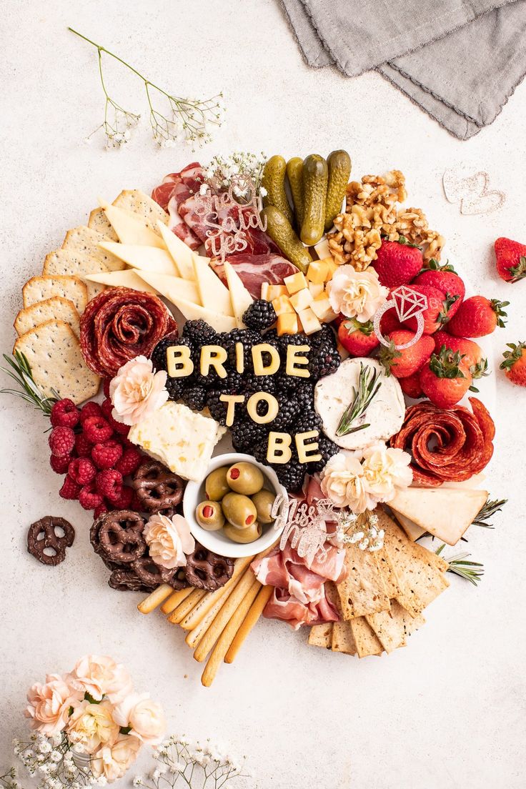 the bride to be board is surrounded by flowers and crackers, olives, strawberries, pretzels