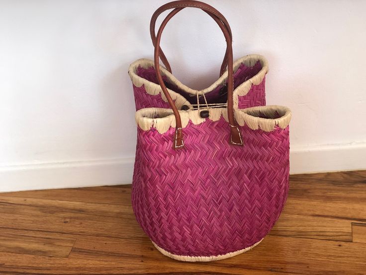 These beautiful pieces are designed in South Africa. Handmade with raffia and featuring leather handles, these bags bring the perfect mix of bohemian chic to everyday wear! Capable of being used as a handbag, basket or storage-this multi-purpose piece is a cannot miss! The double closure top provides a multi-style capability as well! Sizing: 16 inches wide x 12 inches deep x 13 inches high Pink Top Handle Straw Bag For Beach, Pink Bucket Bag With Braided Handles For Shopping, Pink Bucket Bag With Braided Double Handles, Pink Bucket Bag With Double Braided Handles, Pink Bucket Bag With Braided Handles And Top Handle, Pink Double Handle Bucket Bag With Braided Handles, Pink Top Handle Straw Bag For Everyday, Pink Travel Bag With Bamboo Handle, Pink Vacation Bag With Bamboo Handle