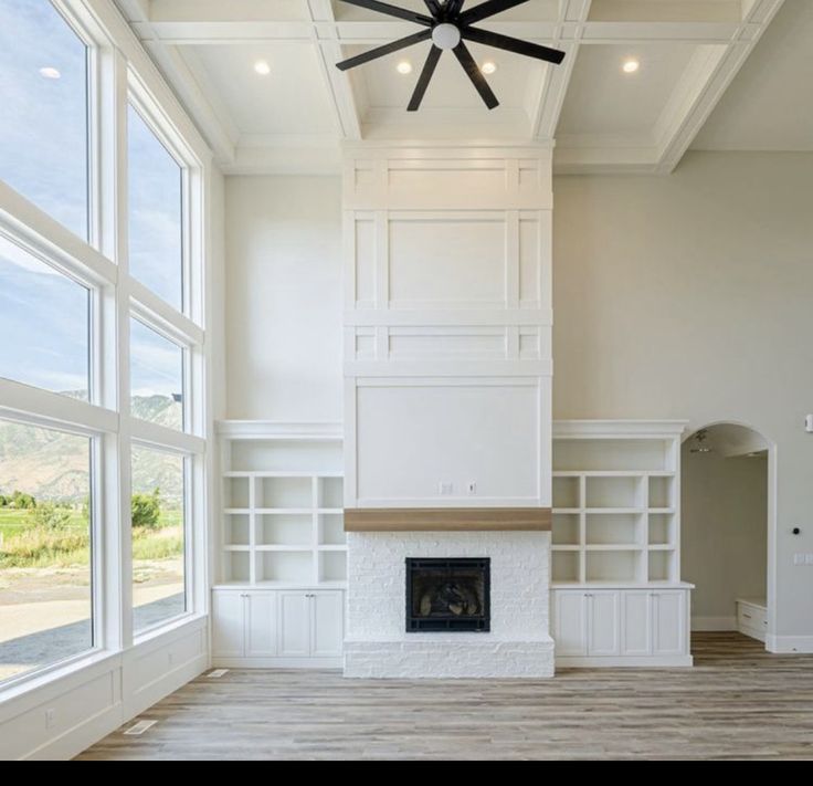 an empty living room with large windows and a ceiling fan in the middle of it