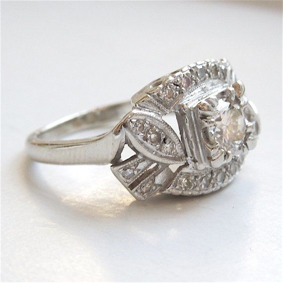 This vintage 1940s ring has a central diamond, weighing approximately 0.50ct (H color, SI2 clarity). An additional 0.25ct of diamonds surrounds the center, and the top of the ring - with the way the mounting is carved and the stones are set - has the illusion of motion. The mounting is made entirely of 14K white gold.SIZE 6.5 (can be sized) Vintage White Diamond Ring With Halo Setting, Vintage Diamond White Diamond Ring With Halo Setting, Vintage Diamond White Ring With Halo Setting, Vintage White Cluster Ring With Rose Cut Diamonds, Vintage Diamond White Diamond Ring For Formal Occasions, Vintage White Rings With Halo Setting, Vintage Platinum Rings With Halo Setting, Vintage Diamond Halo Ring With Rose Cut Diamonds, Vintage White Wedding Ring With Halo Setting