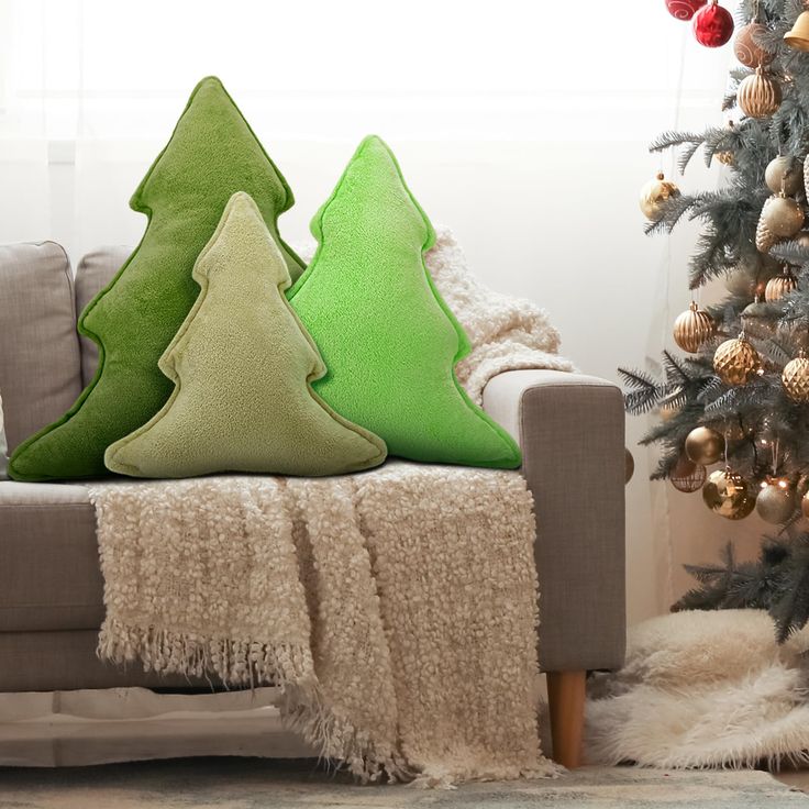 three green christmas trees sitting on top of a couch in front of a christmas tree