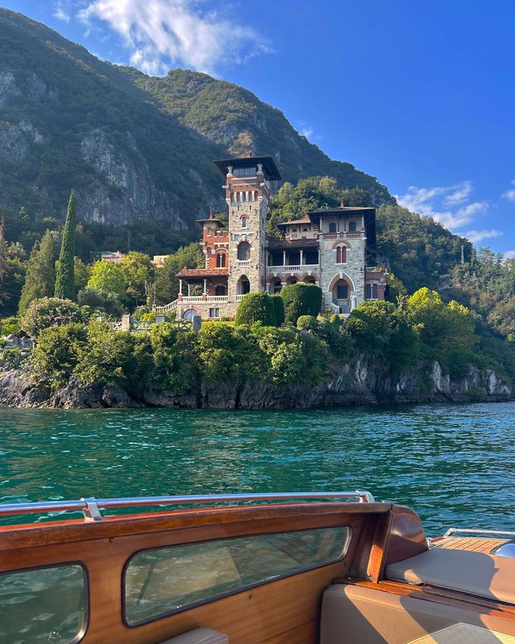 a boat traveling down a river next to a large house on top of a mountain