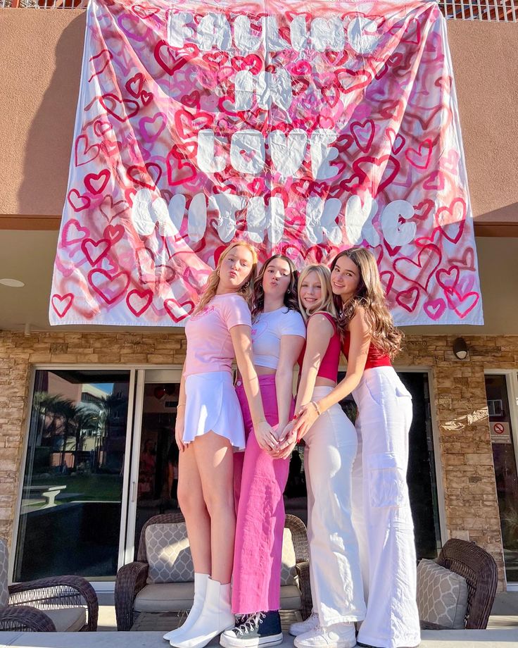 three girls standing in front of a pink heart banner