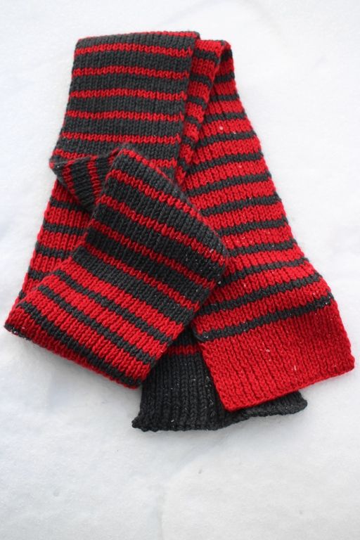 two red and black striped gloves laying on top of each other in the white snow