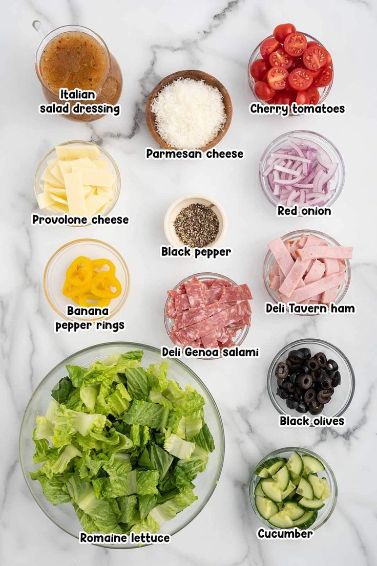 the ingredients to make this salad are shown on a marble counter top, including lettuce, tomatoes, cucumbers, black olives, parmesan cheese and red onion