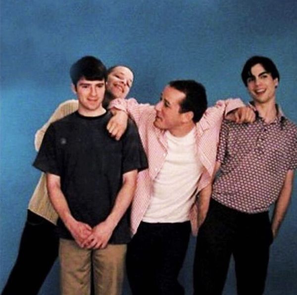 four men are posing together in front of a blue wall