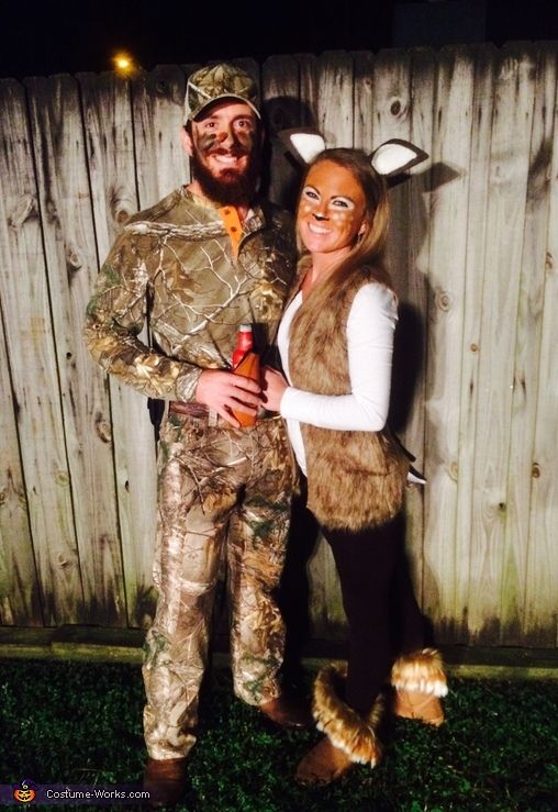 a man and woman dressed up as deer hunters for halloween costumes, standing next to each other in front of a wooden fence