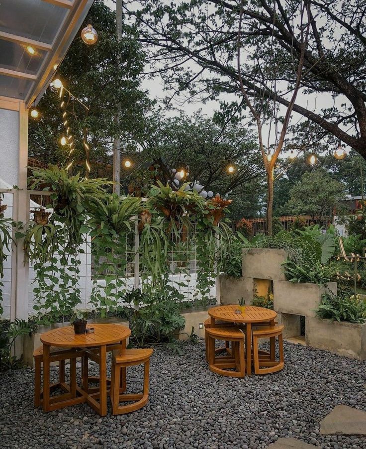 two wooden tables sitting on top of a gravel covered ground next to trees and plants