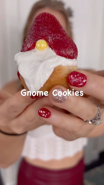 a woman holding up a pastry with white frosting and strawberries on the top