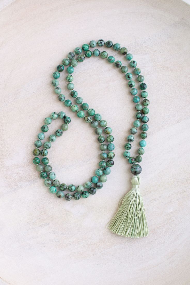 This mala necklace is made with 6-7mm African turquoise beads and a 10mm African turquoise guru bead. The beads are a green turquoise color with a brownish black matrix. Each strand of beads is unique. If you would like a photo of your mala before it is shipped out, please feel free to message me.  This mala is hand-knotted and made in the traditional way with 108 beads. It is 32" in length and the sage green tassel is available as either 2" or 3" long. The tassel is handmade using silk thread.  African turquoise encourages positive change, optimism and balance. It opens the mind to new ideas and helps us confidently walk towards our dreams. African turquoise is part of the jasper family. This mala will come in a stamped cotton bag and box with a card explaining the gemstone meaning. What Green Round Beads Spiritual Crystal Necklace, Jade Bead Necklaces For Meditation, Green Gemstone Beads Mala As Gift, Adjustable Jade Beaded Necklace With 8mm Beads, Spiritual Jade Beaded Necklaces For Meditation, Bohemian Necklaces With 8mm Beads, Bohemian Necklace With 8mm Round Beads, Green Bohemian Necklace With 8mm Beads, Adjustable Spiritual Turquoise Necklace For Meditation