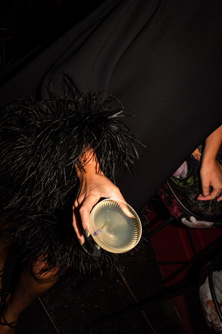 a woman in a black dress holding a frisbee with feathers on her arm