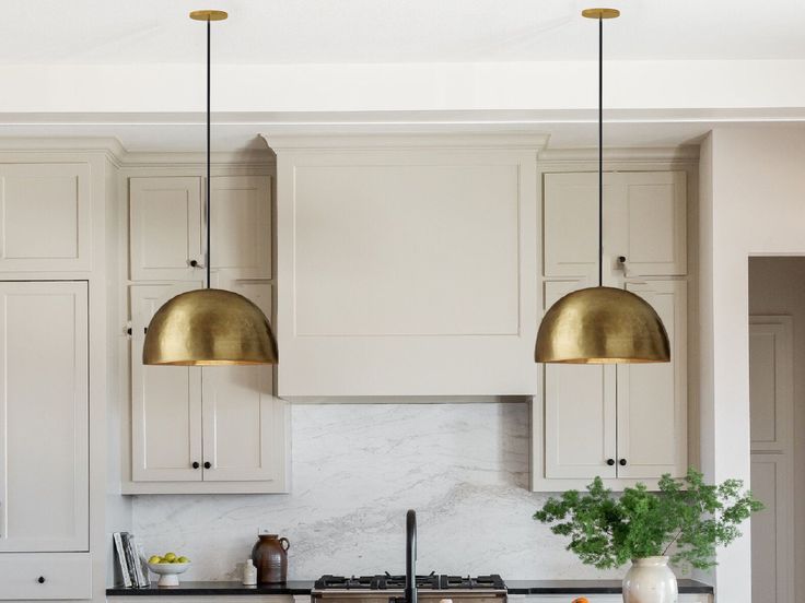 a kitchen with white cabinets and gold pendant lights