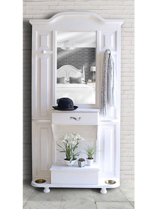 a white shelf with a mirror and some flowers on it in front of a brick wall