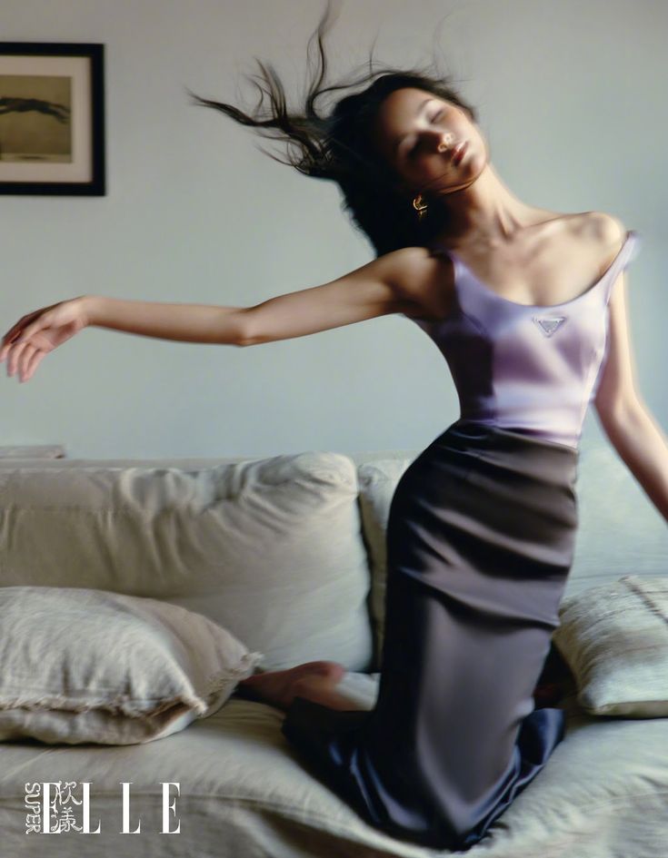 a woman sitting on top of a couch next to a white wall and pillows with her hair in the air