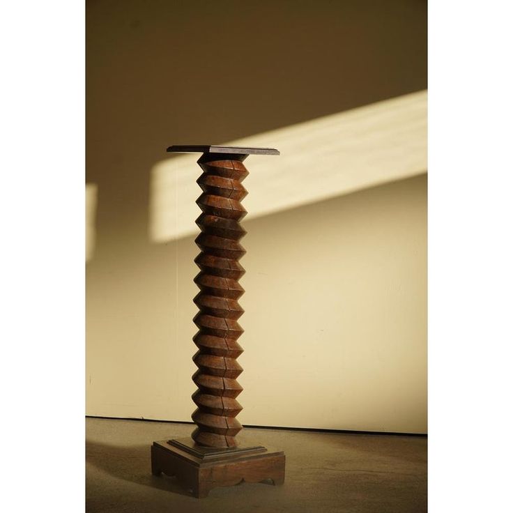 a tall wooden object with a metal top on it's stand in front of a wall