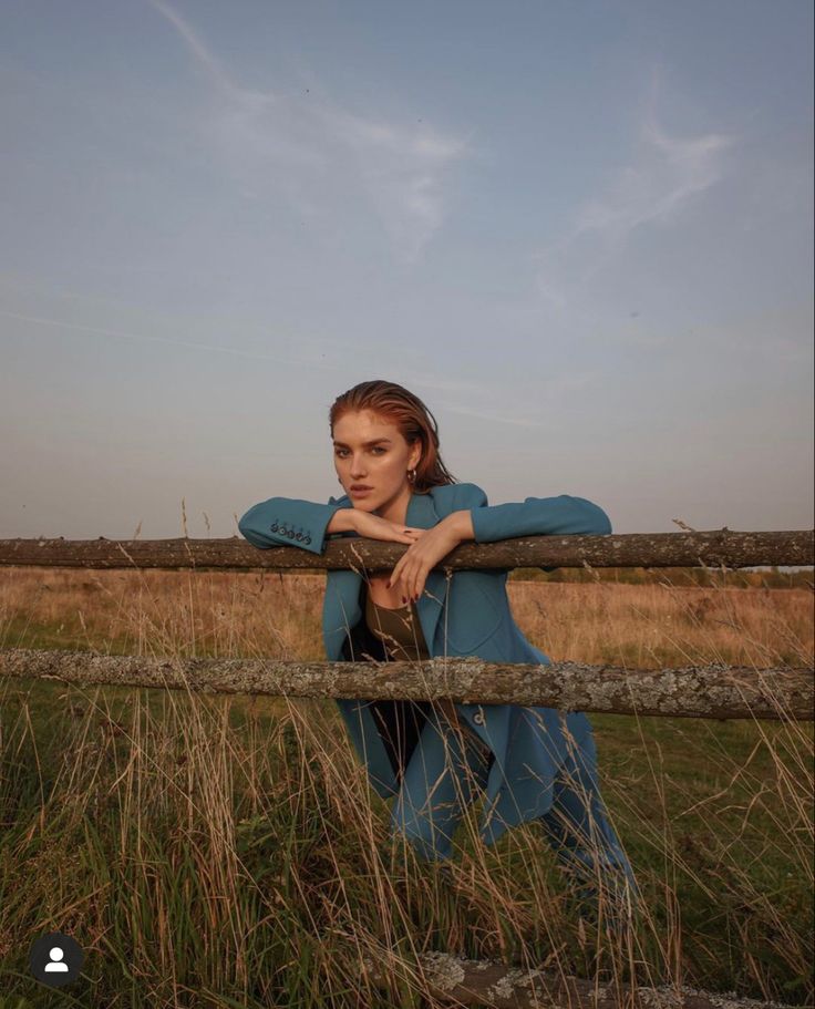 a woman leaning on a fence in a field