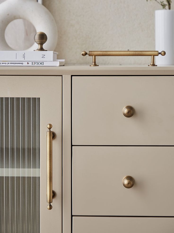 a white dresser with gold handles and knobs on it's drawers next to a book shelf