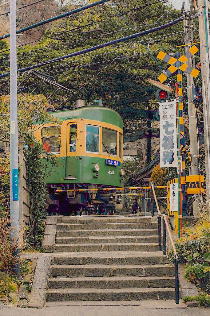 a green and yellow train is coming down the tracks in front of some steps that lead up to it