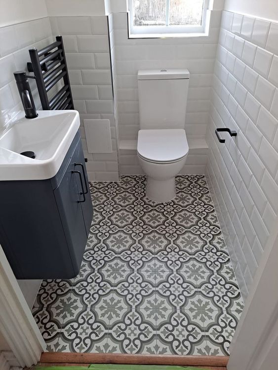 a white toilet sitting next to a sink in a bathroom under a window on top of a tiled floor