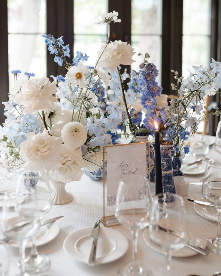 a table with plates, silverware and vases filled with blue and white flowers