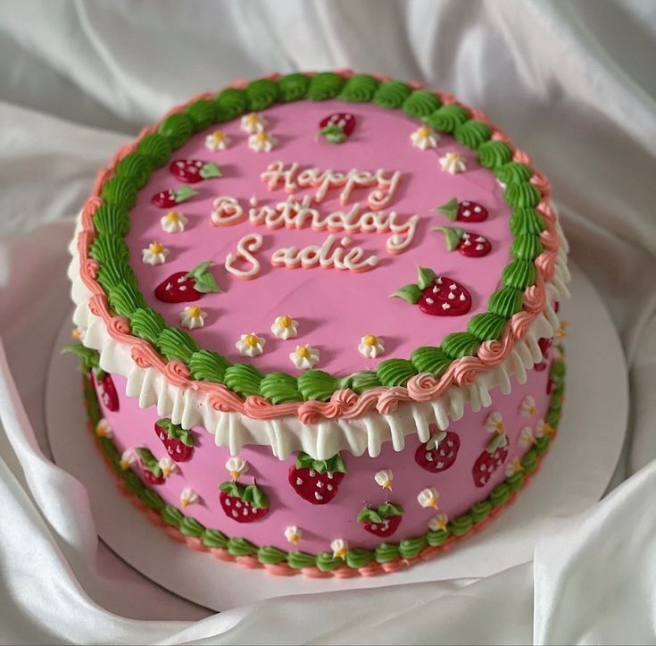 a birthday cake decorated with strawberries and daisies on a white tableclothed surface